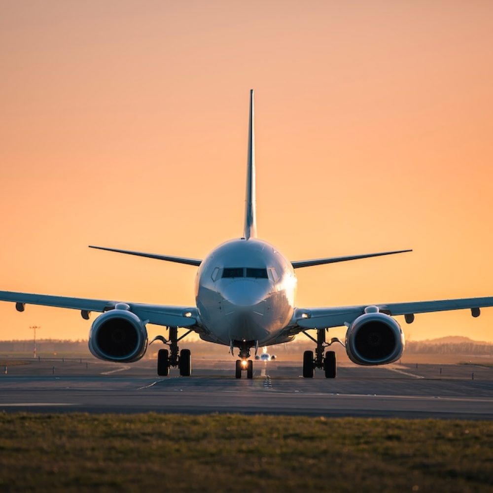 Traffic at airport at golden sunset. Front view of taxiing airplane while other taking off from the runway.